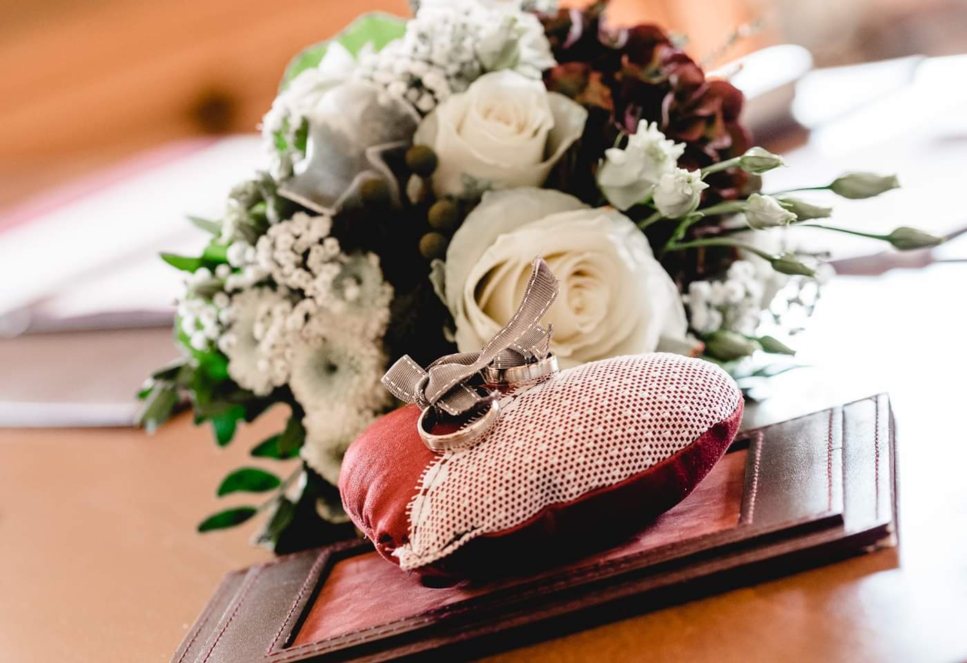 Ein Blumenstrauß und Eheringe auf einem Kissen auf einem Tisch.