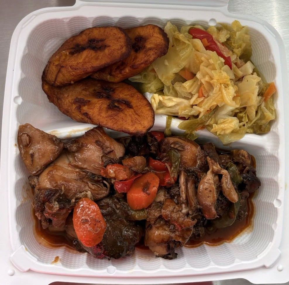 Plate of Caribbean food: jerk chicken, fried plantains, and sautéed cabbage with carrots and peppers.