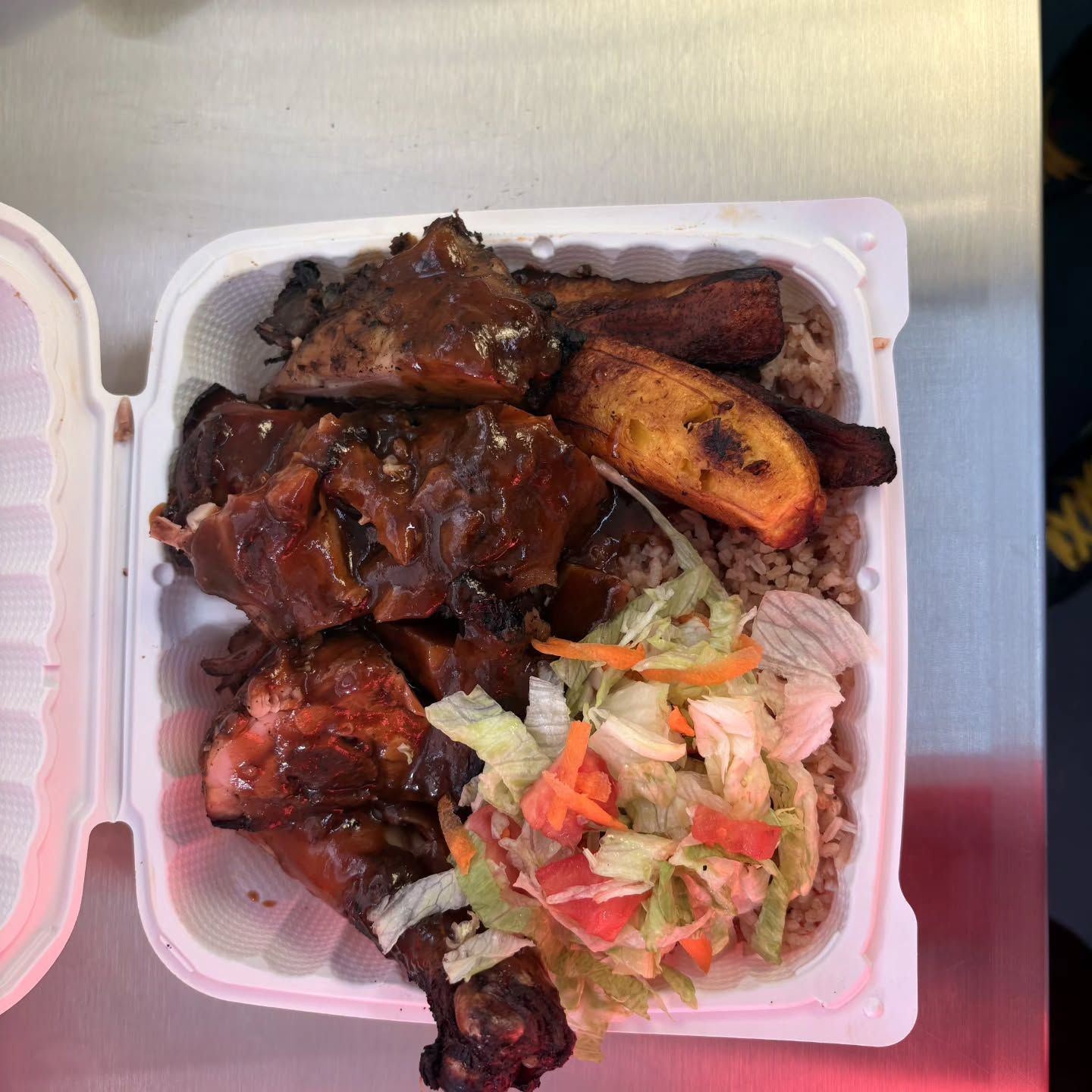 Takeout container with jerk chicken, rice, plantains, and salad.