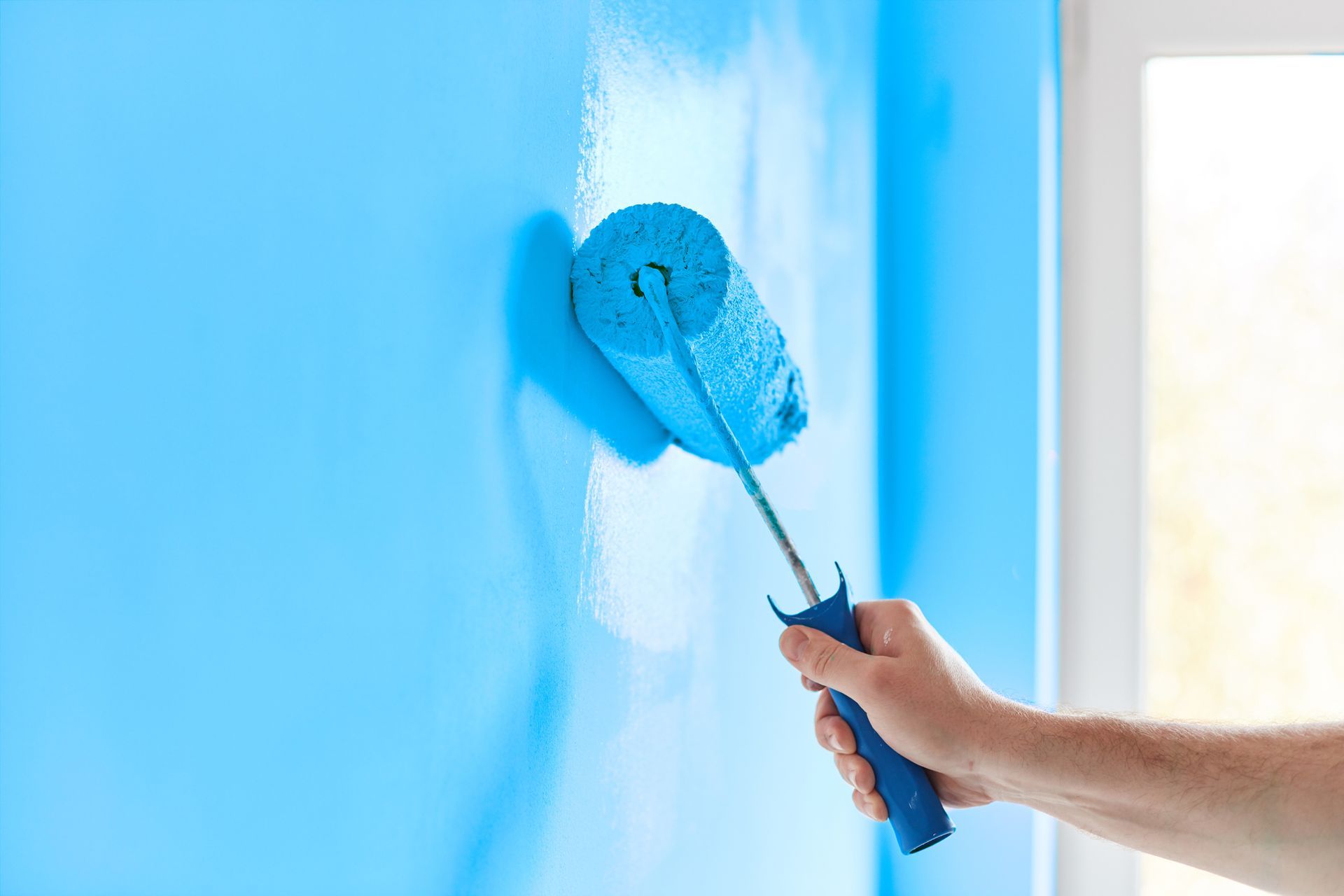 A person is painting a blue wall with a blue paint roller.