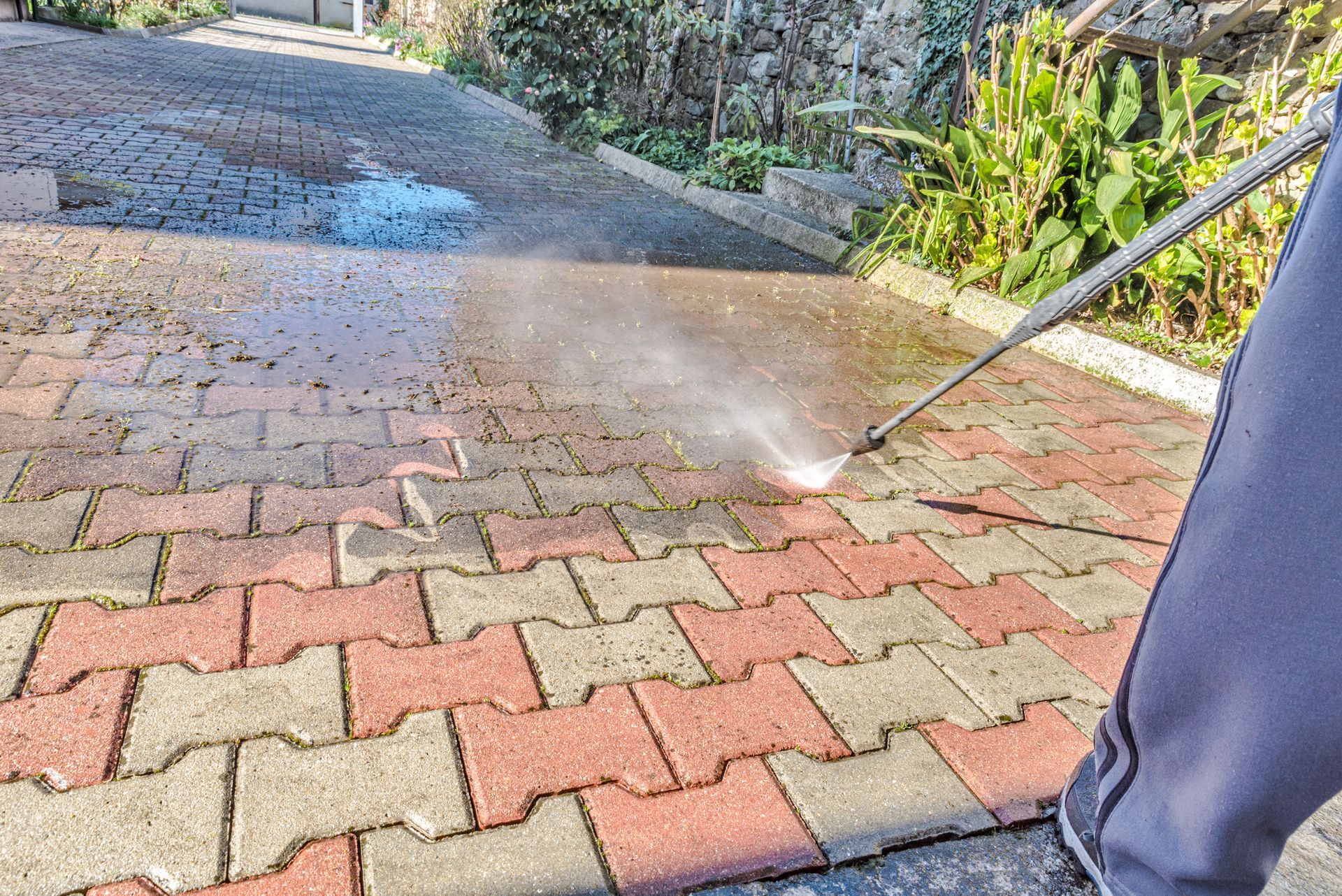 A person is using a high pressure washer to clean a brick driveway.