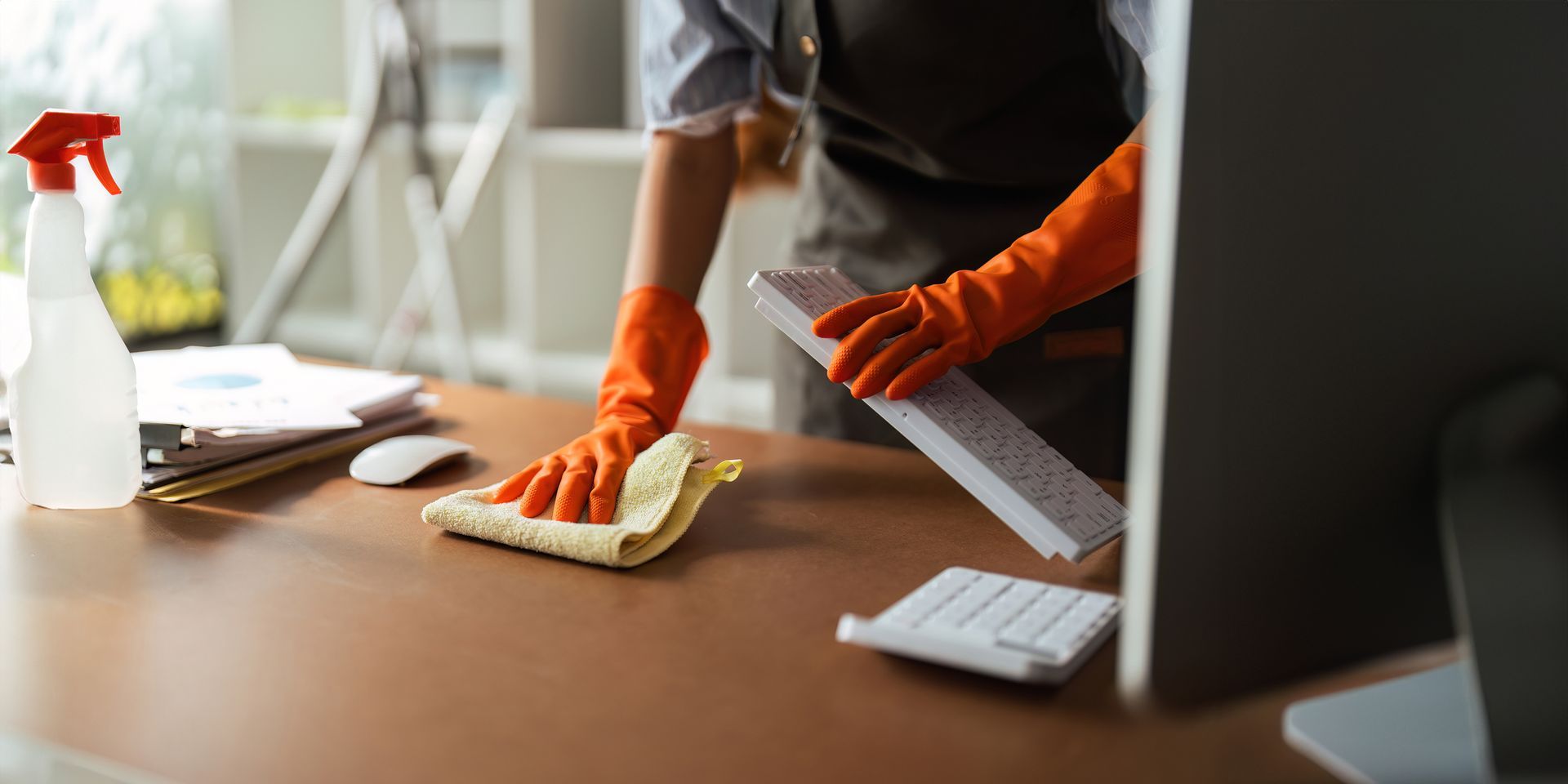 A person wearing orange gloves is cleaning a desk in an office.