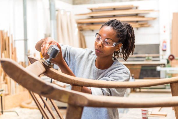 A woman is working on a wooden chair in a workshop.