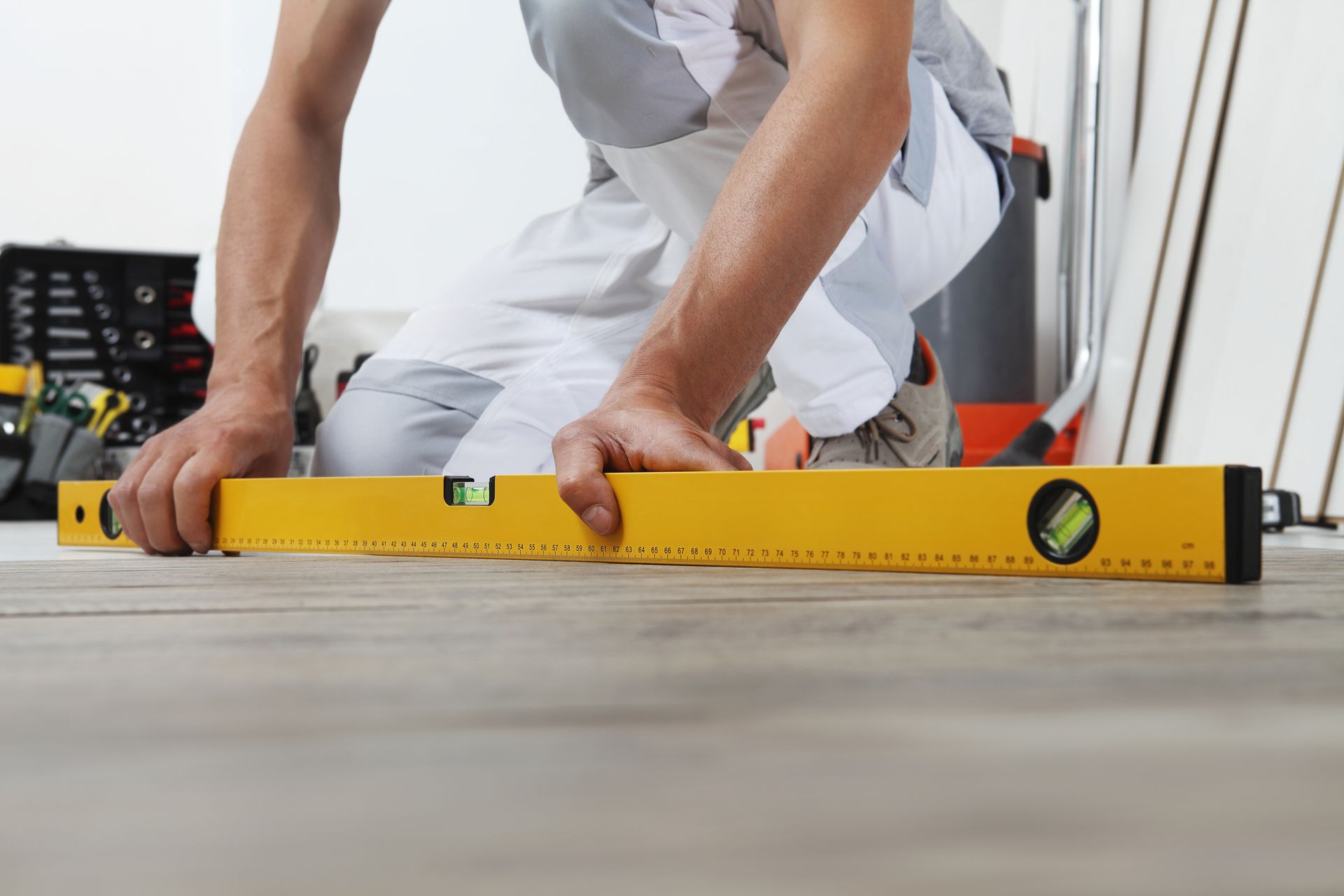 A man is using a yellow level on a wooden floor.