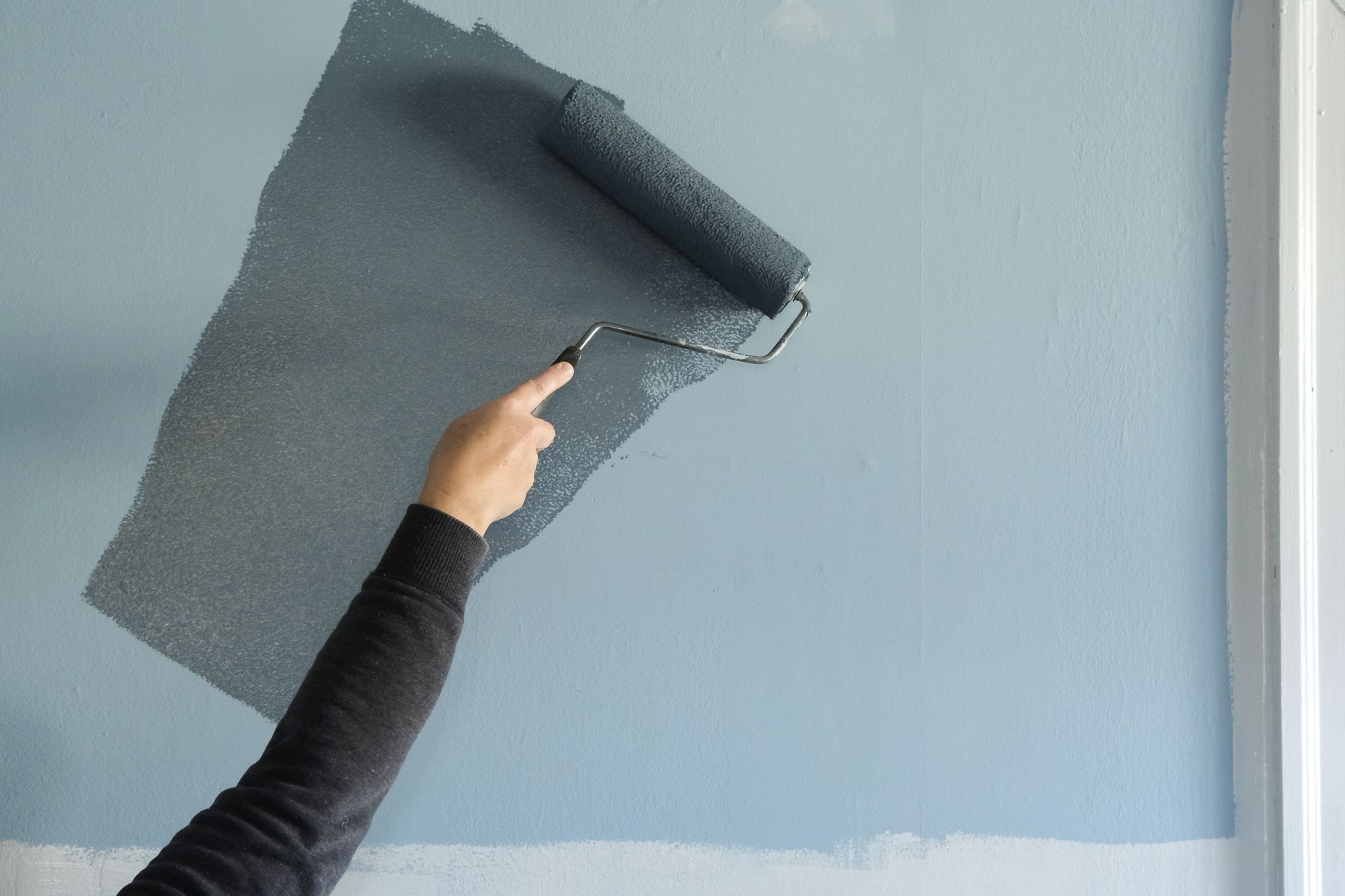 A person is painting a wall with a paint roller.