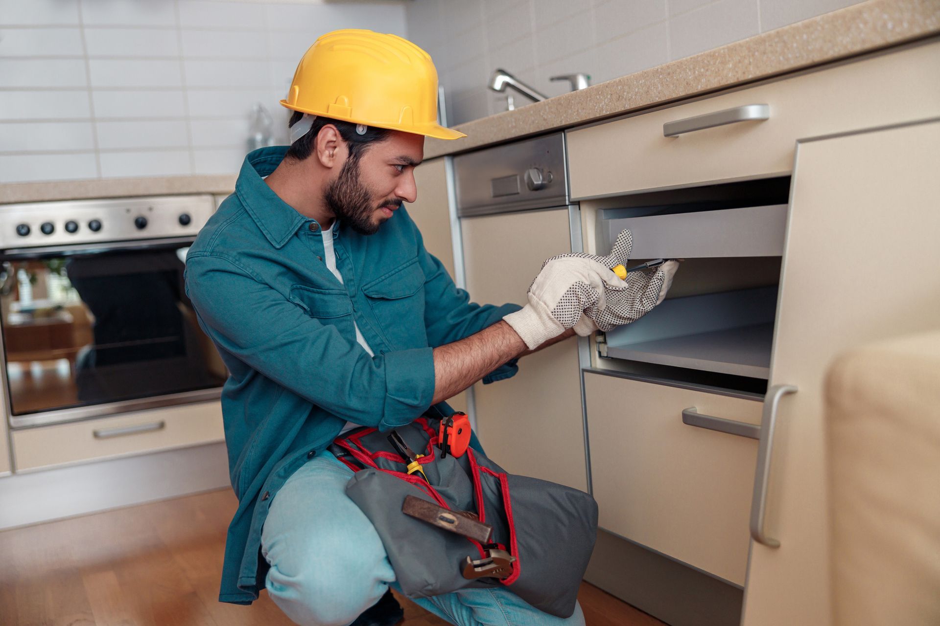 A man is kneeling down in a kitchen looking under a sink.