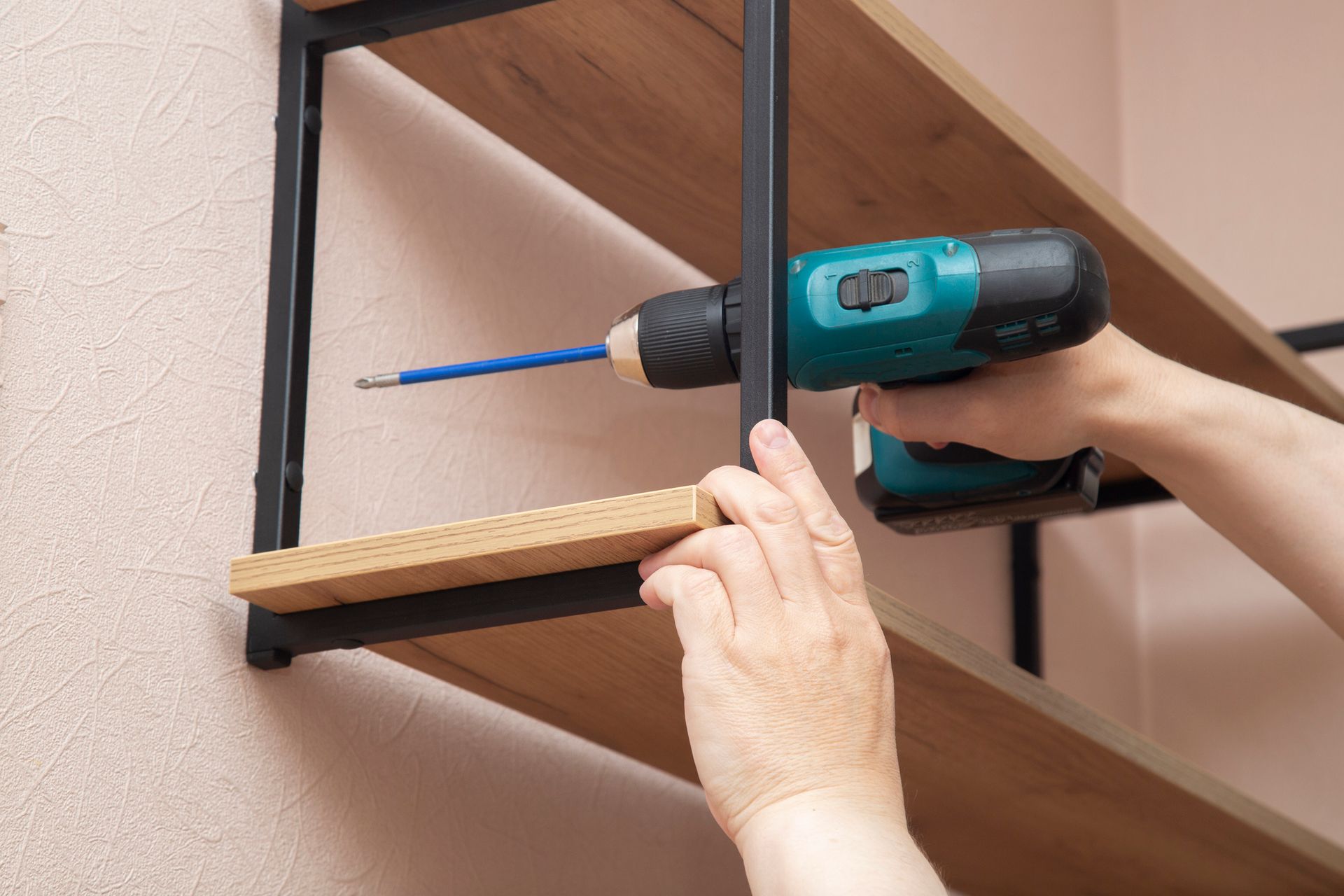 A person is using a drill to install a shelf on a wall.