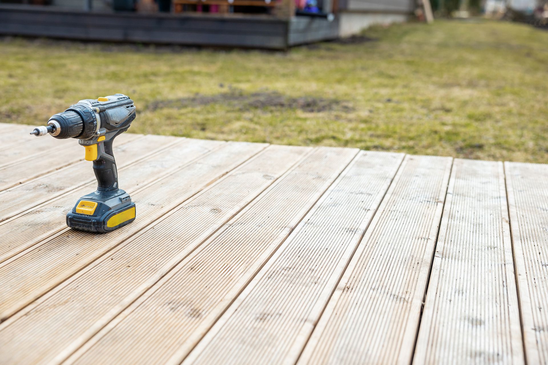 A cordless drill is sitting on a wooden deck.