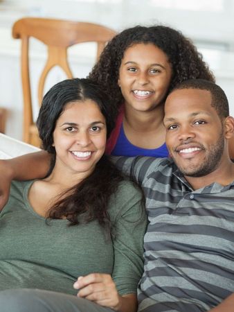 Mom, dad, and teenage daughter smiling on a couch.