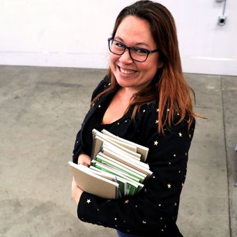 Roya Dedeaux holding notebooks and smiling at the camera.