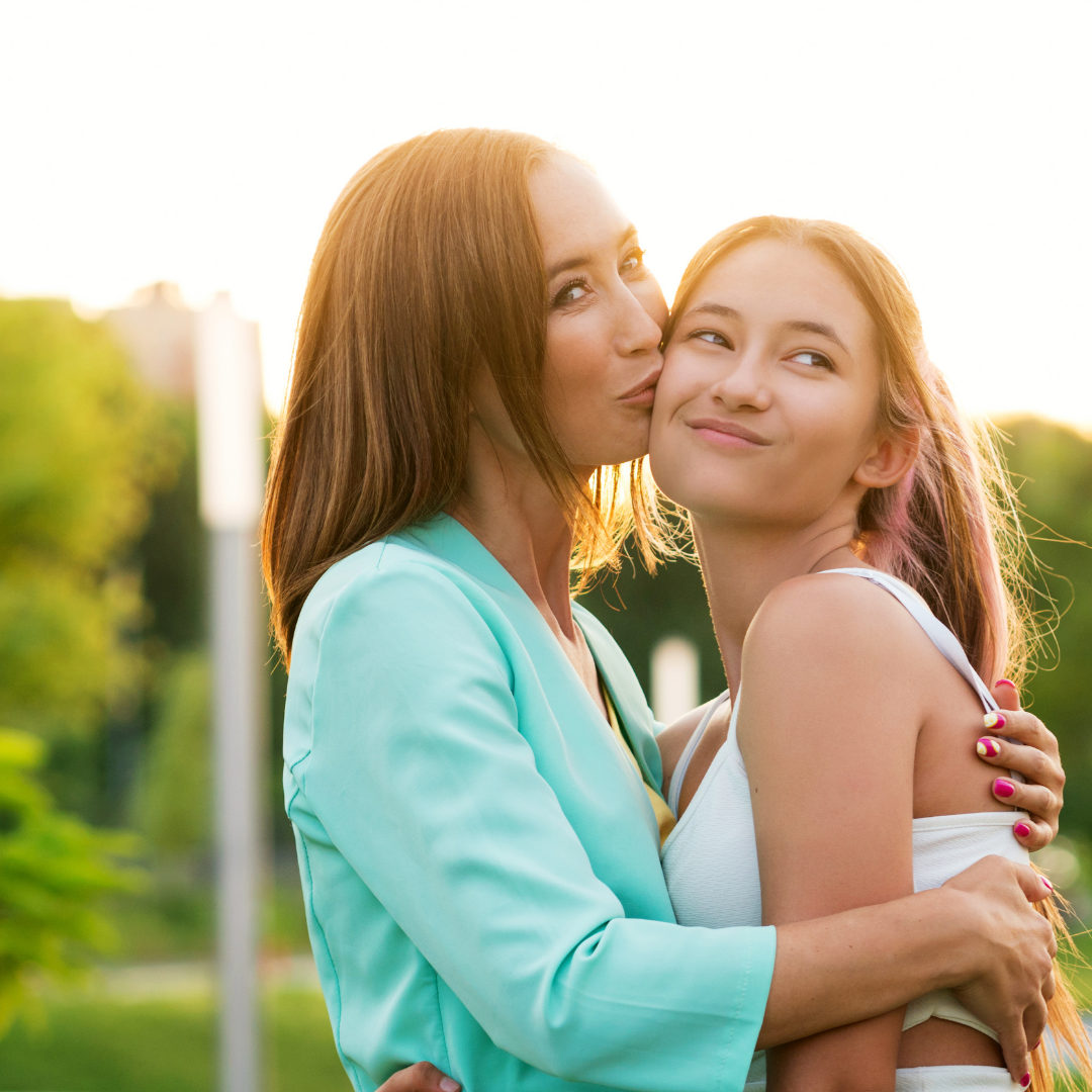 An image of an asian mom kissing her teen daughter on the cheek