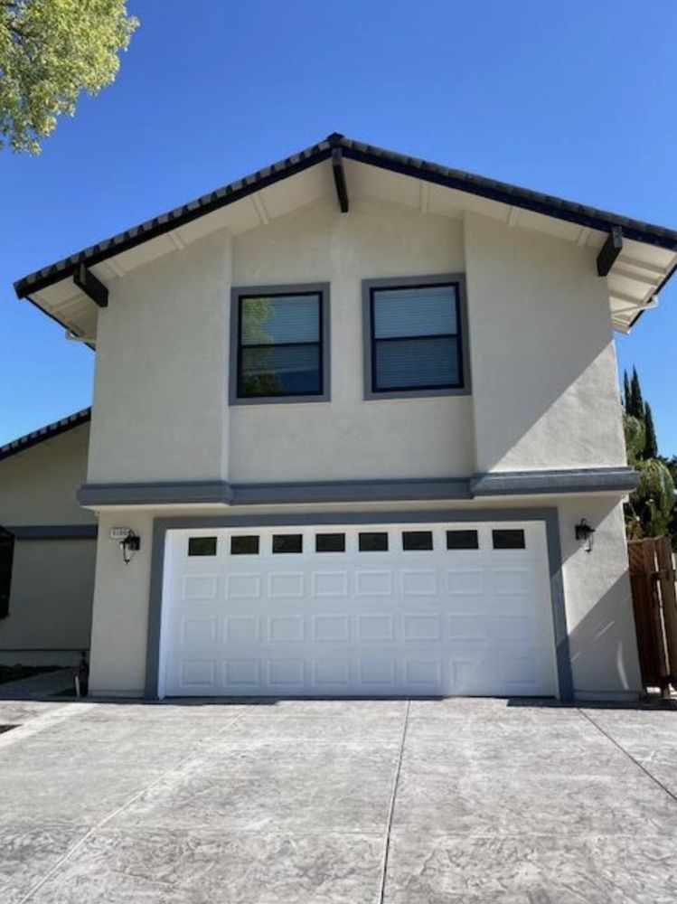 Two-story beige house with white garage door and concrete driveway under a blue sky