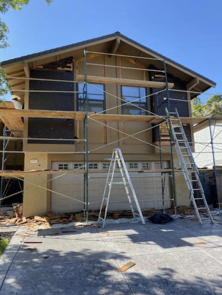 Two-story house under renovation with scaffolding and ladders on the front exterior