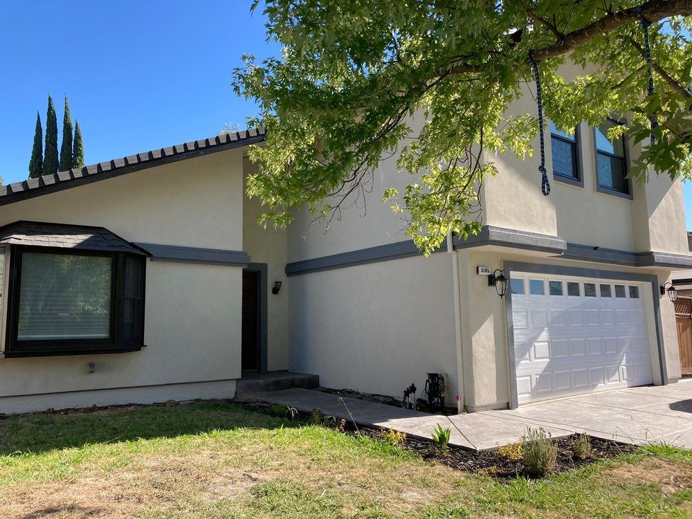Suburban house exterior with cream stucco, white garage, and tree-shaded front yard