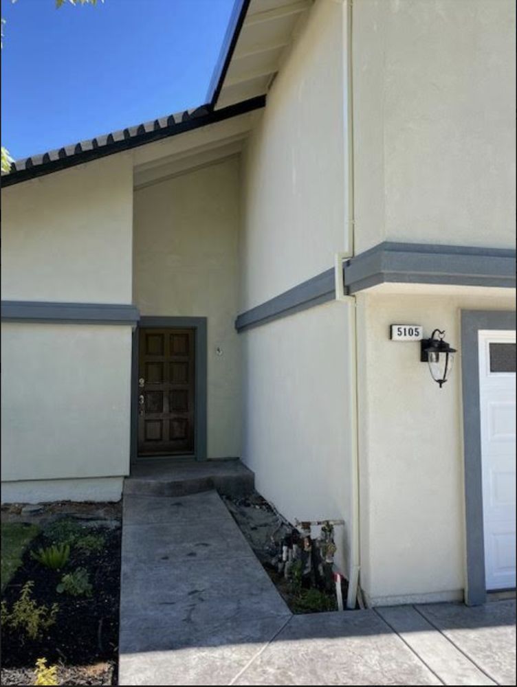 Front entry walkway to a cream stucco house with gray trim and a wooden door under a blue sky