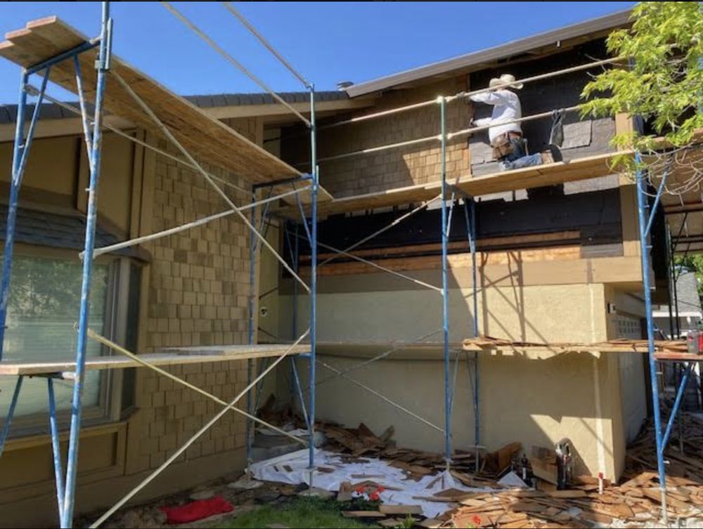 Scaffolded house exterior under construction, with workers on the upper level and building materials below