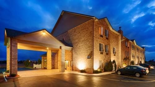 Lit brick building at dusk with illuminated entrance and parked cars outside.