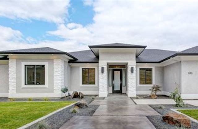 Modern single-story white house with black roof and front walkway under a cloudy sky