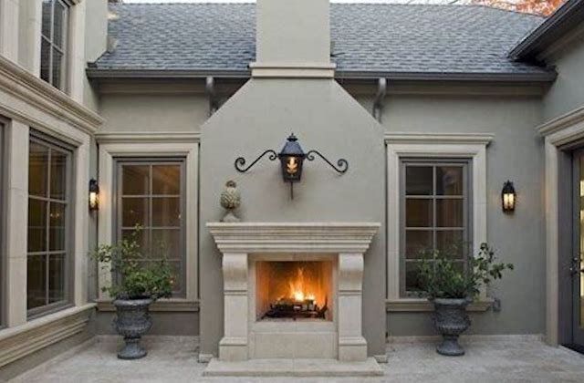 Courtyard patio with a lit outdoor fireplace, twin windows, and potted plants beneath a stucco wall