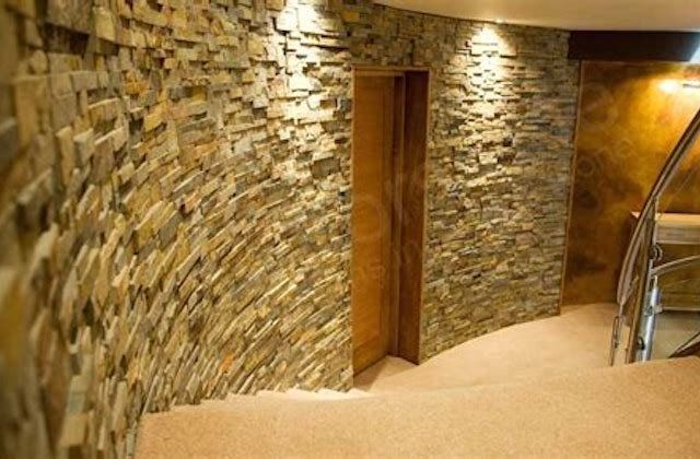 Curved stone hallway with wooden doorway and glass-railed stairway, warmly lit indoors