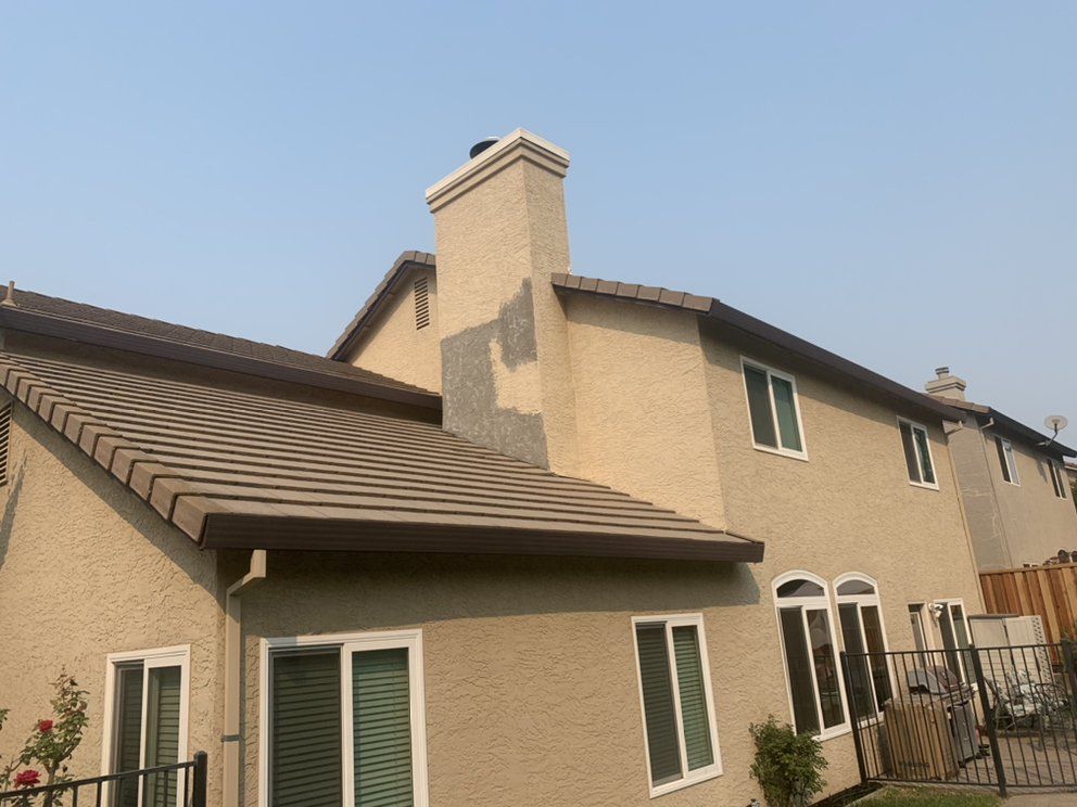 Suburban stucco house with tan walls, brown roof, and white-framed windows under a clear sky