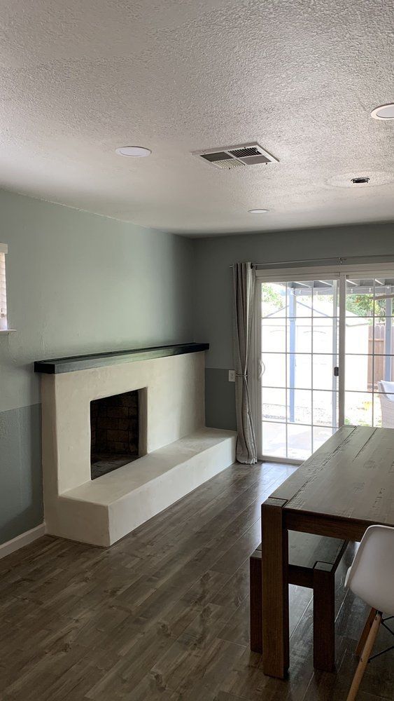 Empty modern living room with fireplace, gray walls, wood floors, and sliding glass doors leading outside