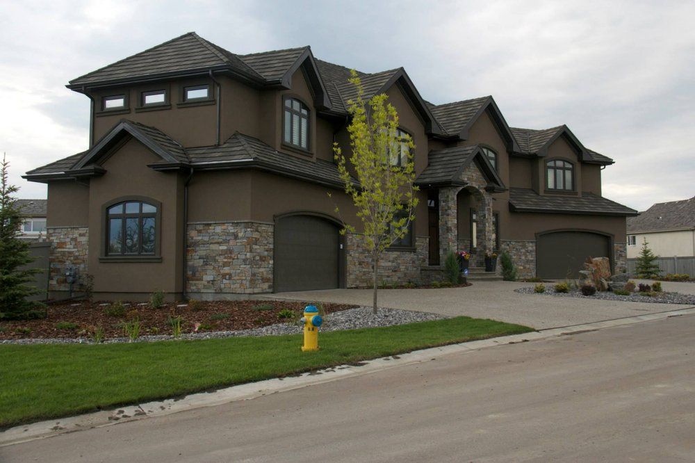 Large brown suburban house with stone accents, front lawn, and driveway under a cloudy sky