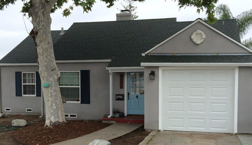 Gray house with blue front door, white garage, and large tree in front yard
