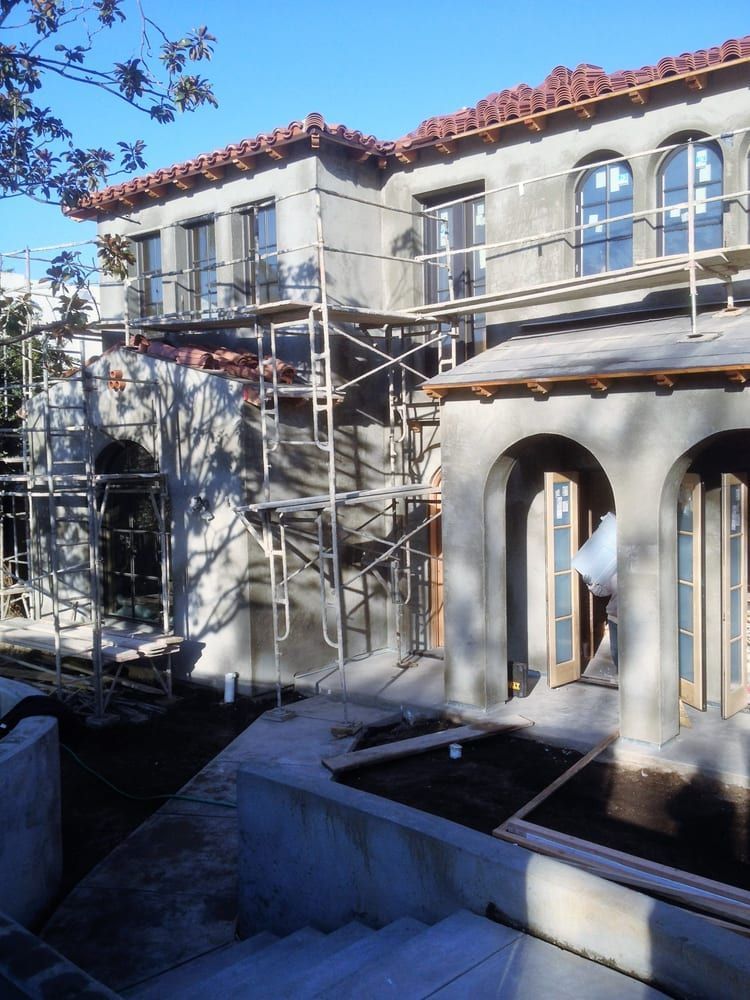 Scaffolding on a stucco house with arched windows and red-tile roof under construction
