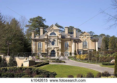 Grand stone mansion with ornate facade, front gardens, and fountain under a clear blue sky