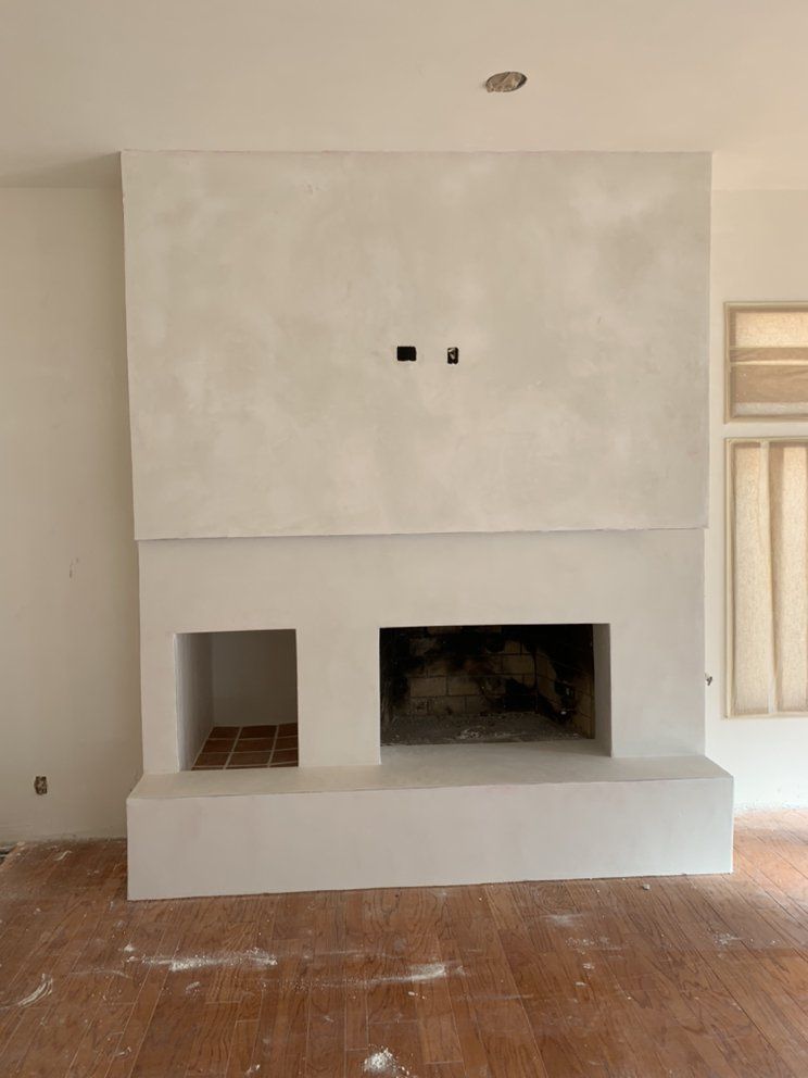 Modern unfinished fireplace with white plaster surround and a dusty floor in a bare room