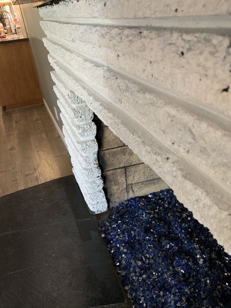 White textured fireplace mantel with exposed brick hearth and a dark floor mat in a room