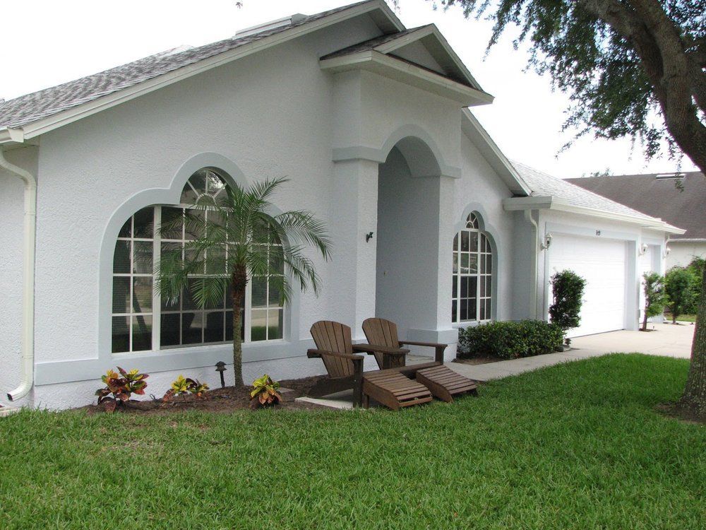 White suburban house with arched windows, front lawn, and patio chairs on a covered porch