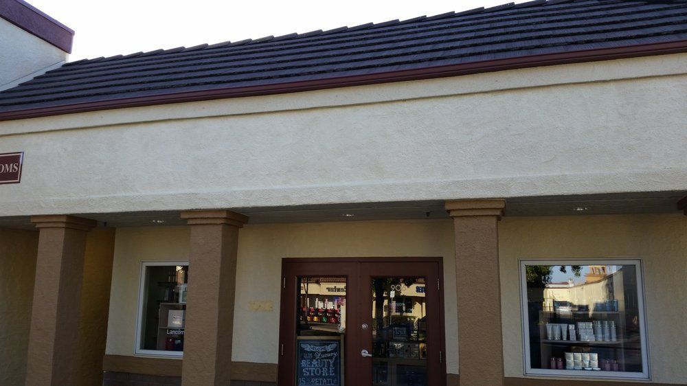 Storefront with tan stucco walls, dark roof tiles, and double glass doors between two windows.