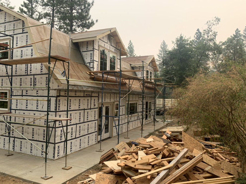 House under construction with scaffolding, wrapped exterior, and a pile of lumber in front