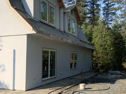 Two-story gray house exterior with deck and forested backyard