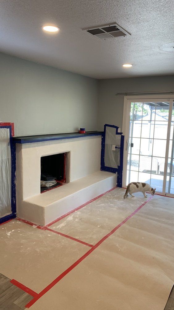 Living room under renovation with floor covered in plastic and red tape, fireplace, and sliding glass door.
