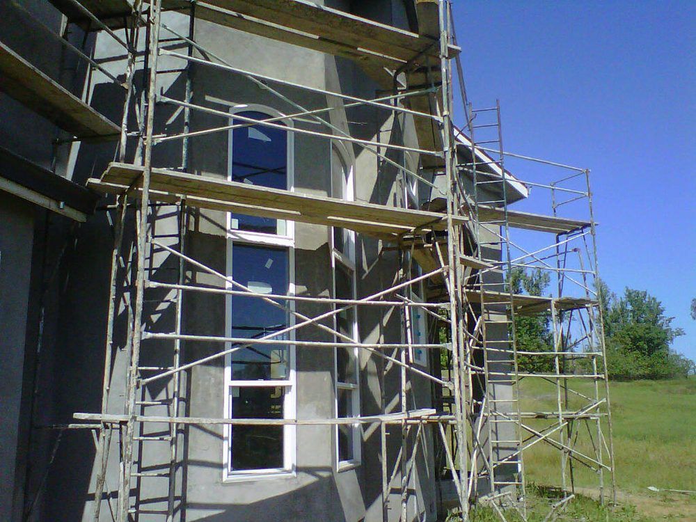 House exterior with scaffolding and ladders during construction under a clear blue sky