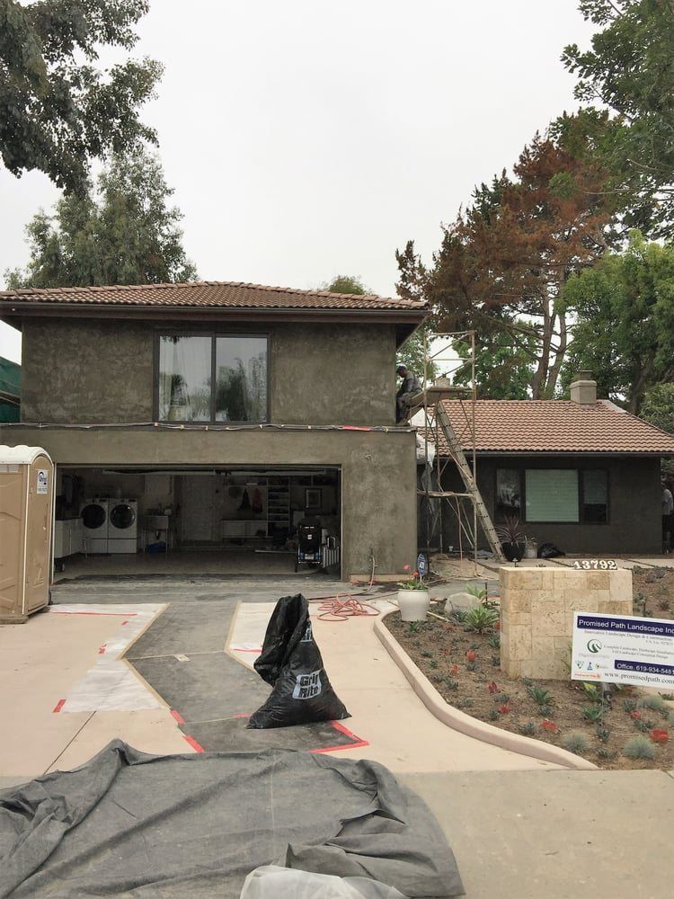 Two-story house with open garage, driveway construction materials, and ladder under cloudy sky