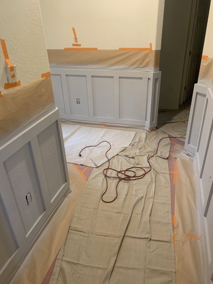 Kitchen under renovation with white cabinets, orange tape, and drop cloths covering the floor