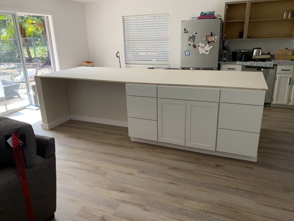 Kitchen with a long white island, light wood floors, gray cabinets, and a refrigerator by a window.