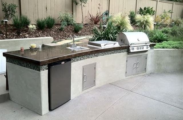 Outdoor patio kitchen with sink, grill, and granite countertop built into a stone island.
