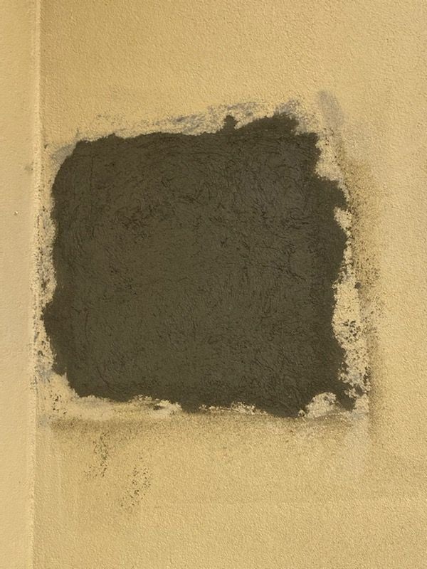 Dark gray patch of paint or plaster on a beige wall