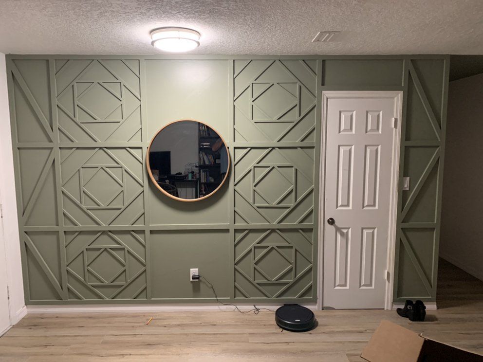 Green paneled wall with round mirror, white door, ceiling light, and a few items on the floor.