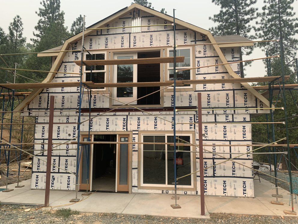Two-story house under construction with scaffolding and roof framing, wrapped in weatherproof sheathing.