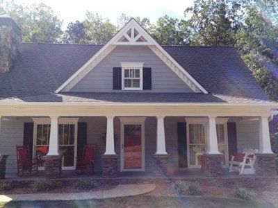 White farmhouse with porch, black shutters, and steep gabled roof on a sunny day