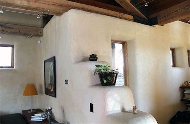 Rustic living room with white stucco walls, wood beams, framed art, lamp, and a small window shelf with plants