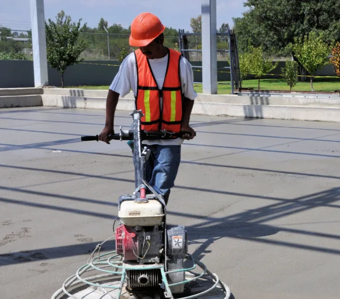 A man wearing an orange vest and hard hat is using a machine