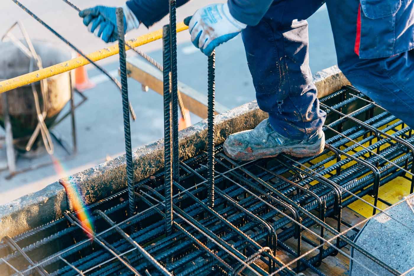 A construction worker is welding metal bars on a concrete floor.