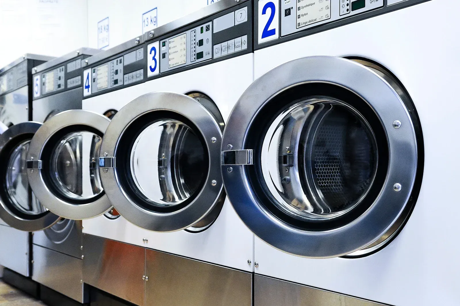A row of washing machines in a laundromat with the doors open.